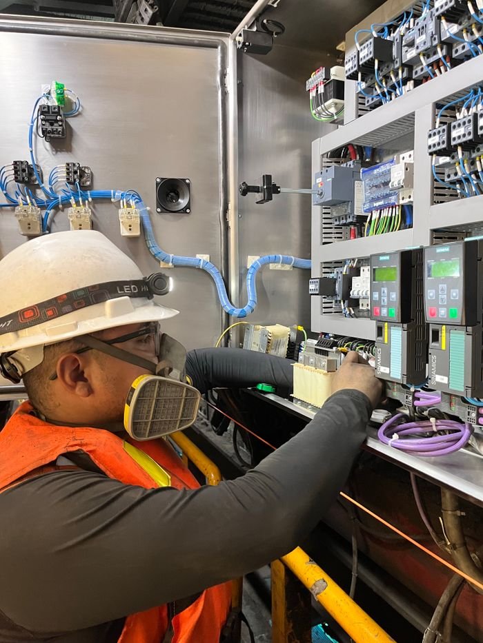 Electrician wearing safety gear adjusting wires on a control panel in Callao, Perú.